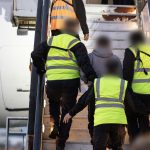IMG_5184 - The Afghan Times People in neon safety vests boarding an aircraft via exterior stairs, hands on rails, blurred faces for privacy.