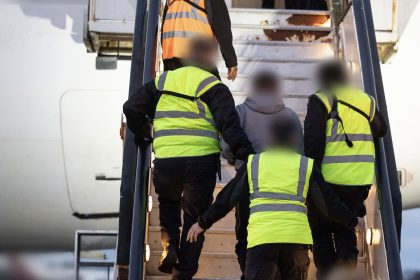 People in neon safety vests boarding an aircraft via exterior stairs, hands on rails, blurred faces for privacy.