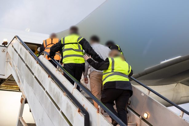 Ground crew members in high-visibility vests ascend an external aircraft stairway toward the plane.
